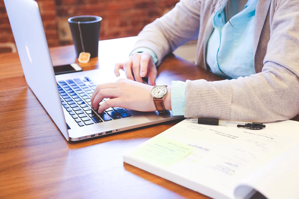 Person working on a desk with a laptop, a notebook, and a cup of coffee